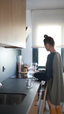 Sabah ışığında, genç bir kadın modern ve rahat mutfağında kahvaltı hazırlamakla meşgul.