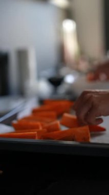 İyi aydınlatılmış bir mutfakta taze havuçları bir tepside dizerken, yemek pişirmeye hazırlanan ellerin yakın çekimi..