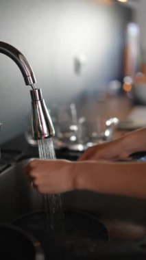 Mutfak lavabosunda bulaşıkları akan suyla yıkayan ellerin yakın çekimi. Musluklu temiz mutfak sahnesi.