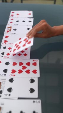 Bir masanın üzerine dizilmiş iskambil kağıtlarının yakın çekim sekansı ve onları elinde tutan bir kişi, devam eden bir oyunu gösteriyor.
