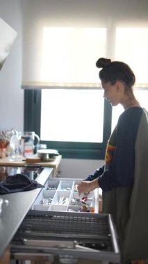 Bir kadın, modern bir evin mutfak çekmecesini günlük ev işlerini takip ederek sabah güneşinin altında düzenliyor.