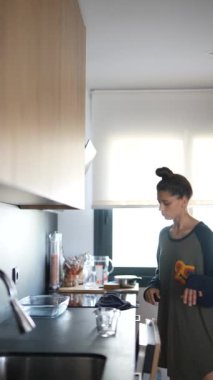 Günlük giysiler giyen bir kadın, ev işlerini gösteren, çağdaş bir mutfakta bulaşık makinesini doldururken görülüyor.