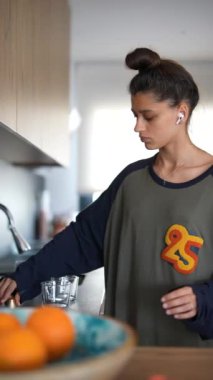 Kulaklık takan genç bir kadın modern bir mutfakta sabah kahvesini yudumlarken rahat ve rahat bir hava yayıyor.