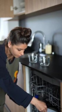 Genç bir kadın mutfak dolaplarını düzenliyor ve bulaşık makinesini dolduruyor.