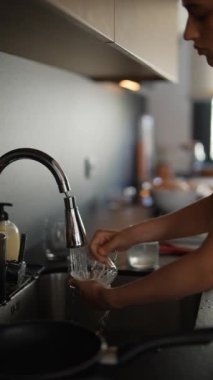 Modern bir mutfakta bir kadın bulaşıkları yıkıyor, günlük ev işlerini akan suyla yapıyor, temizliğini koruyor.