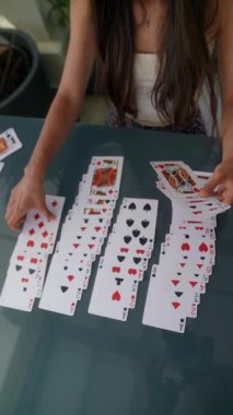 Bir kadın cam masanın üzerinde kartlarla bir solitaire oyunu kuruyor, dört deste oluşturuyor ve dikkatlice düzenliyor.
