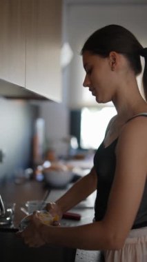 Genç bir kadın modern bir mutfakta, evinde temizlik ve hijyeni sağlamak için bulaşıkları yıkıyor.
