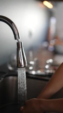 Modern bir mutfak lavabosunda akan musluğun altında ellerini yıkayan bir insan.