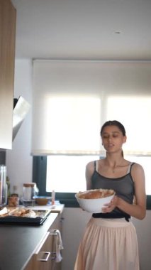 Modern bir mutfakta, genç bir kadın parlak ışık ve ahşap dolaplarla çevrili ev yapımı yemekler pişiriyor.