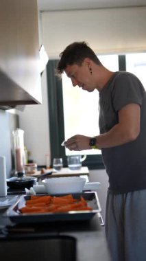 Modern bir mutfakta havuçla sağlıklı bir yemek hazırlayan bir adam. Yemek pişirmeye ve fırın kullanmaya odaklanmış..