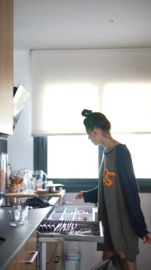 Parlak bir mutfakta, büyük bir kazak giyen bir kadın kahvaltı hazırlar, şık bir sabah rutini sergiler.