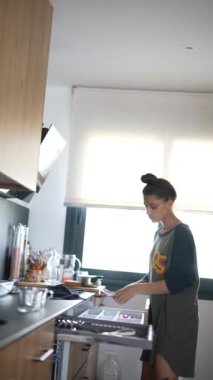 Modern bir mutfakta, günlük giysiler içindeki genç bir kadın basit ve verimli bir ortamda yemekleri rahat bir şekilde hazırlar.