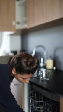 Bir kadın mutfak düzenliyor. Bulaşıkları kaldırarak ve rahat bir ev ortamında dolapları düzenleyerek..