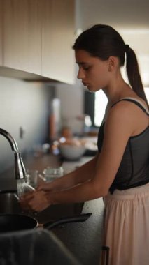 Çağdaş bir mutfak ortamında, bir kadın ev işlerinin bir parçası olarak lavaboda bulaşık yıkamaya odaklanır.