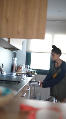 Modern bir mutfakta, bir kadın mutfak aletleri düzenler, düzenli bir yaşam tarzıyla etkin bir evi yansıtır.