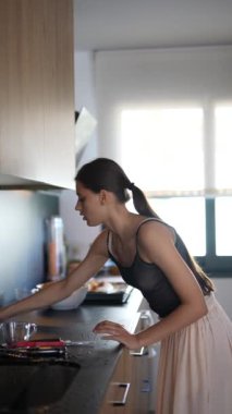 Bir kadın modern bir ortamda mutfak tezgahını süngerle temizliyor, ev işlerini hallediyor.