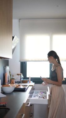 Genç bir kadın, yeni pişmiş hamur işleriyle aydınlık ve modern bir mutfakta mutfak çekmecesi düzenliyor..