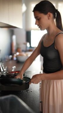 Genç bir kadın modern bir mutfakta yemek pişiriyor ve bulaşıkları yıkıyor, ev işlerini ve günlük rutinlerini gösteriyor..