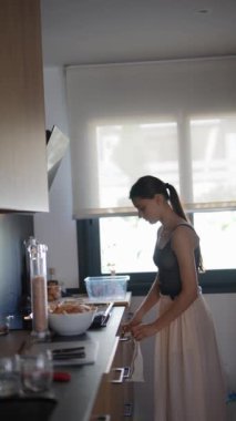 Modern bir mutfakta, bir kadın günlük rutininin bir parçası olarak yemek hazırlar ve ev işlerini yönetir.