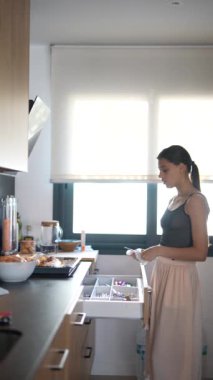 Genç bir kadın, modern bir evde günlük kıyafetleriyle mutfak aletlerini topluyor.