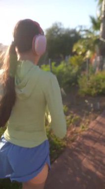 Kulaklıklarla koşan genç bir kadının arka planda güneşli bir günün tadını çıkarması..