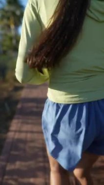 Genç bir kadın güneşli bir günde spor giysileri içinde koşuyor ve müzik dinlemek için kulaklık kullanıyor.