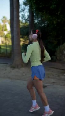 Spor kıyafetleri ve kulaklıklı bir kadın parkta koşuyor. Sağlıklı bir açık hava yaşam tarzını gösteriyor.