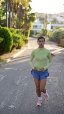 Yeşil bluzlu ve mavi şortlu bir kadın banliyö caddesinde koşuyor, yemyeşil bir yer
