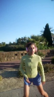 Bir kadın parkta kulaklıklarla koşuyor, güneşin altında egzersiz yapıyor ve güzel bir açık hava manzarası seyrediyor.