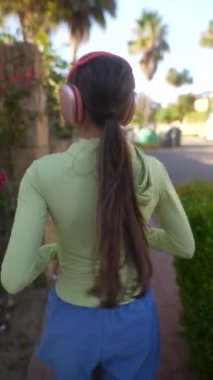Yeşil bluzlu ve mavi şortlu bir kadın kulaklıkla dışarıda koşuyor. Anahtar sözcükler egzersiz, fitness, sağlıklı yaşam tarzı