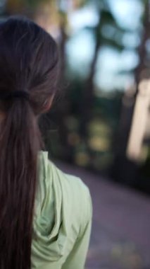 Yeşil ceketli, uzun saçlı bir kadın dışarıda geziyor, güneş ışığında güneşleniyor ve doğayla iç içe.