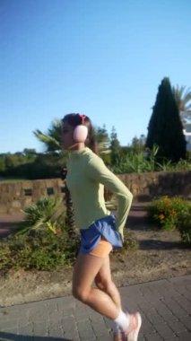 Genç bir kadın güneşli bir günde dışarıda koşmaktan hoşlanır, kulaklık takar ve spor kıyafetleri giyer..