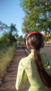 Kulaklıkla koşan biri açık gökyüzü ve yemyeşil ile güneşli bir günün tadını çıkarıyor..