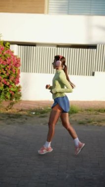 Yeşil bluzlu ve mavi şortlu bir kadın açık havada egzersiz yapıyor, güneşli bir günde sağlıklı bir hayat sürüyor.