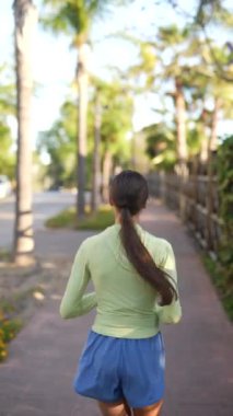 Formda bir kadın, ağaçlar ve ahşap çitlerle çevrili bir parkta koşar ve dışarıda sağlıklı bir egzersizin tadını çıkarır..