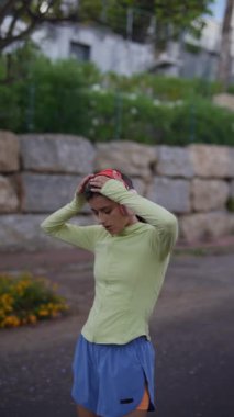 Parlak spor kıyafetleri içinde genç bir kadın doğa yolunda koşuya ara veriyor, aktif yaşam tarzını gösteriyor.