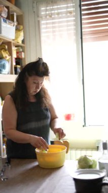 Işıl ışıl bir mutfakta yemek hazırlayan bir kadın, yemek pişirme etkinliğini gösteren malzemelerle dolu bir masa hazırlıyor.