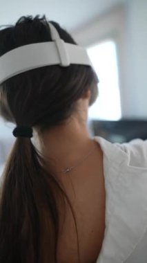 Bir kadın evde sanal gerçeklik deneyimine kendini tamamen kaptırmış vaziyette bir VR kulaklık ve kumanda kullanıyor..