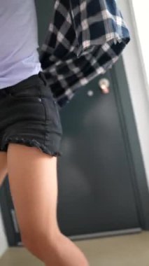 Neşeli genç bir kadın enerjik bir şekilde evdeki kapalı gri bir kapının önünde dans ediyor, neşe ve neşe ifade ediyor.