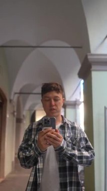 Genç bir adam kareli bir gömlekle tarihi bir koridorda kendi portresini çekmekten mutlu.
