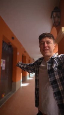 Genç adam sevinçle kollarını açıyor, turuncu bir mimari ara sokağın günlük kıyafetlerinin keyfini çıkarıyor..