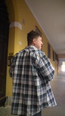 Ekose gömlekli bir adam elinde akıllı bir telefonla tarihi bir binada eski bir koridorda yürüyor.