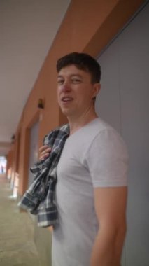 Turuncu duvarlı bir koridorda, ekose gömlekli ve hava podlu genç bir adam rahat bir hava yayıyor.