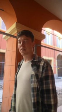 Genç bir adam ekose gömlek ve günlük giysiler içinde şehir mimarisi sergilenen şehir atari salonlarının altında poz veriyor..