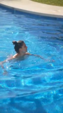 Bir kadın güneşli gökyüzünün altında açık mavi bir havuzda yüzmekten hoşlanır. Yaz tatili için mükemmel bir andır.