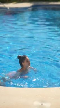 Güneşli bir günde, açık mavi bir havuzda, çeşitli açılardan çekilmiş ferahlatıcı bir yüzüşten zevk alan bir kadın..