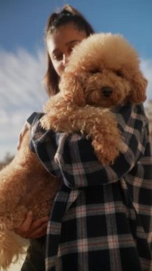 Güneşli bir günde, arka planda açık mavi gökyüzü olan tüylü kanişini mutlu bir şekilde tutan genç bir kadın..