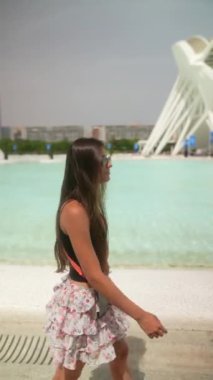 Fütürist mimarisi olan modern bir havuz kenarında yürüyen şık kıyafetli genç bir kadın..