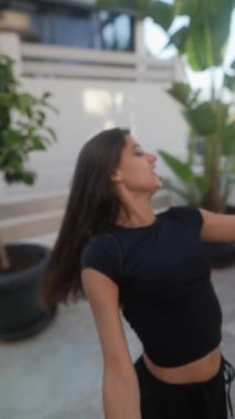 Siyah elbiseli genç bir kadın açık hava aktivitelerine katılıyor. Mavi bir topla, dinamik hareketler sergiliyor..