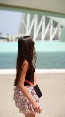 Uzun saçlı ve etekli şık bir genç kadın modern mimari yapıların yakınında geziniyor.